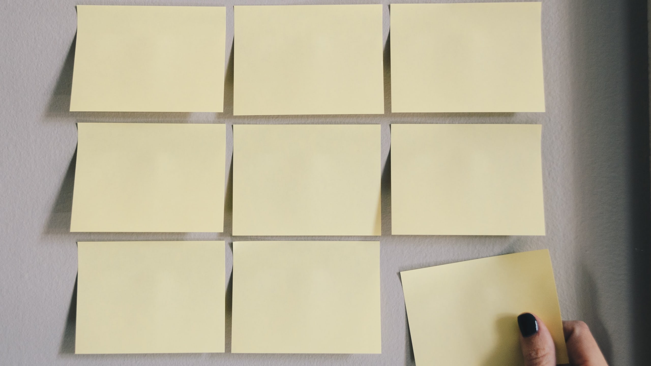 Blank Post-It notes affixed to a wall. A hand is taking one of them off