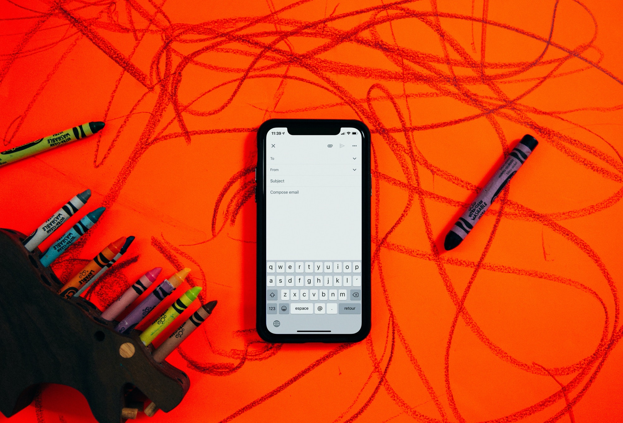 Phone showing an email app resting on a red table covered in crayon drawings