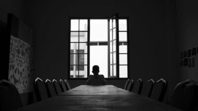Silhouette of a person sitting at an empty table with an open window behind them